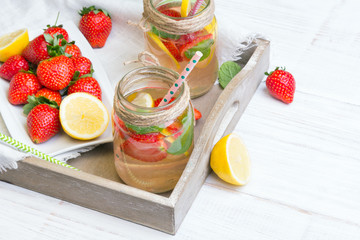 Mineral  water with fresh strawberries, lemon  and mint in jar on a white wooden background, copy space