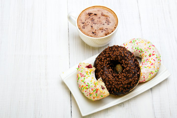 Cup of coffee and tasty donuts with icing and chocolate on white wooden background, copy space