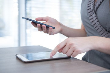 Mid section of female executive using digital tablet and mobile phone at table