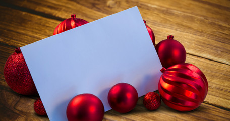 Red christmas baubles surrounding white page against textured wooden floor