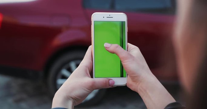 Close up hands woman holding use white phone with green screen background red car scrolling pages swiping surfing internet technology smartphone chroma key message mobile phone sunny sunlight