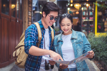 Couple Of Travelers Using Map For Sightseeing In Town. Portrait Of Young Smiling Tourist Man And Woman Holding Map In Hands, Walking On Street And Traveling Together. High Resolution.