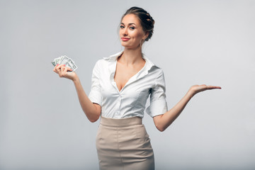 Obraz premium beautiful european business woman in office clothes holding dollars in her right hand and holding her left hand open