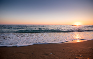 Beautiful sunset wide angle shot of waves slowly splashing on a sandy beach with a couple of round pebble stones, relaxing vibe