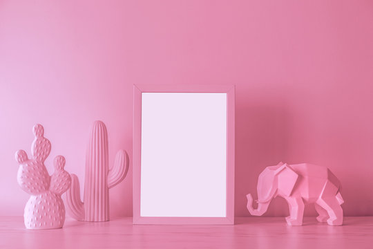 The design pink desk with cacti, elephant figure and photo frame. Modern mock up concept and lightbox concept.