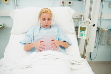 Pregnant woman lying on a hospital bed while holding her belly