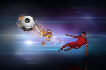 Football player in red kicking against black background with spark