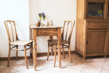 Vintage interior design of kitchen space with small table against white wall with simple chairs and plant decorations. Minimalistic concept of kitchen space.