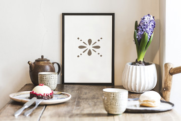 Wooden kitchen table with dessert, tea cups, flower, and mock up frame