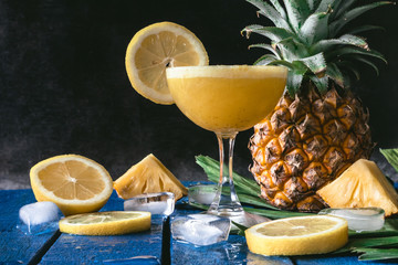 Pineapple smoothie with lemon on blue wooden table, black background