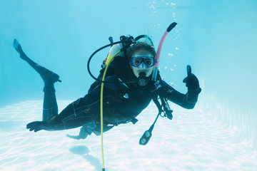 Woman on scuba training submerged in swimming pool showing thumbs up