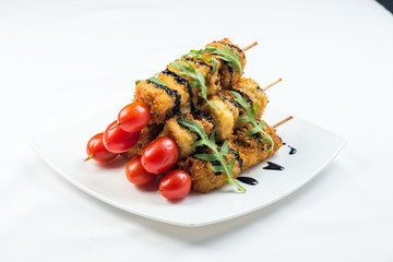 vegetables on skewer fried in batter decorated with tomatoes zucchini, eggplant, zucchini. white plate on white background