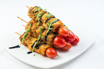 vegetables on skewer fried in batter decorated with tomatoes zucchini, eggplant, zucchini. white plate on white background