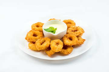 Squid rings fried in batter with white sauce on white plate on white background