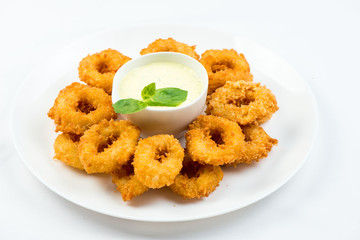 Squid rings fried in batter with white sauce on white plate on white background
