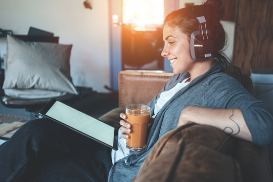 Smiling pretty woman reading tablet pc and listening music, cozy studio apartment