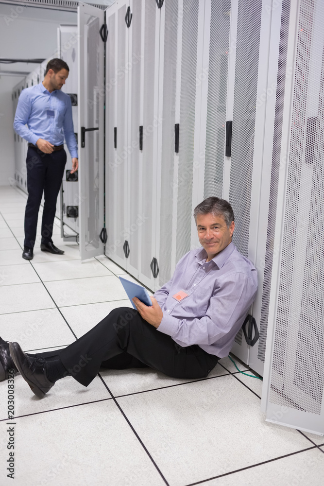 Poster smiling technician using tablet pc sitting on floor