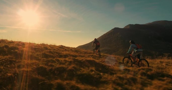 Tracking shot of two mountain bikers riding up hill in amazing sunset light.