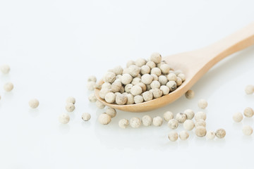 White pepper in wooden spoon on a white background, top view