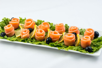 salmon snack on lettuce leaf with lemon and olives on white plate on white background