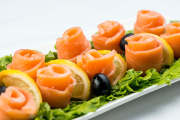 salmon snack on lettuce leaf with lemon and olives on white plate on white background