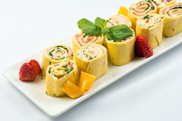 Rolls of thin pancakes with smoked salmon, horseradish cream cheese and rocket leaves on white plate on white background