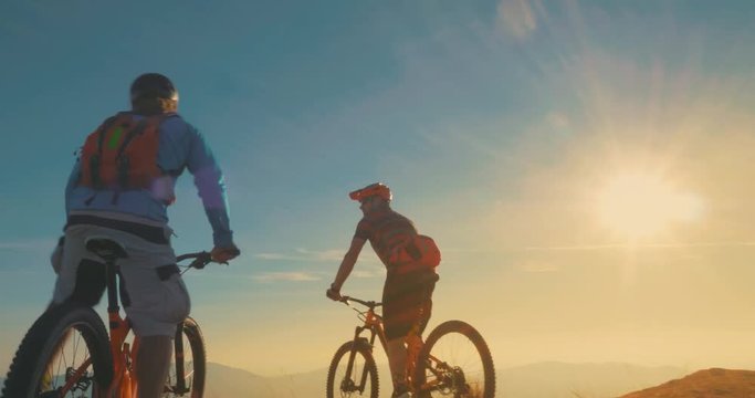 Two mountain bikers reaching the top celebrating with high five in beautiful evening light.
