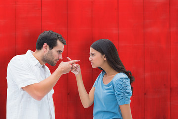 Angry couple pointing at each other against red wooden planks