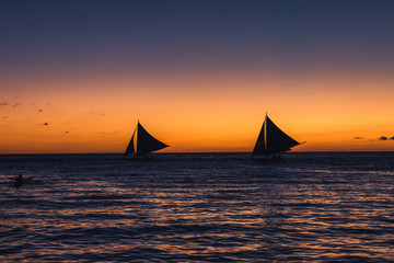 Two outrigger sailboats on the horizon