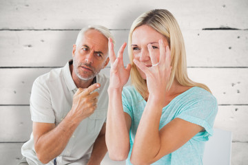 Unhappy couple sitting on chairs having an argument against white wood