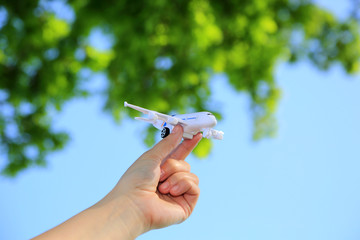 Samolot zabawka w dłoni dziewczyny na tle błękitnego nieba i zielonych liści. - obrazy, fototapety, plakaty