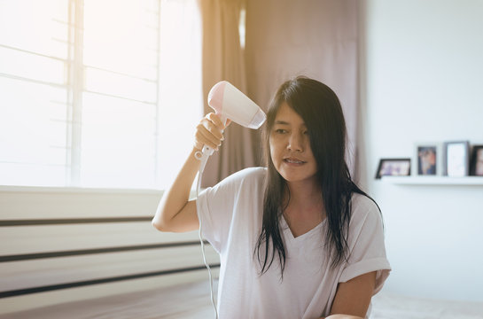 Young asian woman drying her long hair with dryer