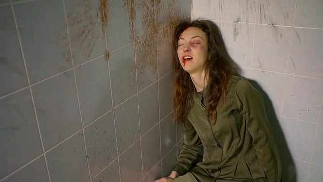 girl with bruises and blood on face is laughing under drugs, touching tiled walls, alcohol intoxication