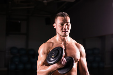 Fototapeta na wymiar Sporty man doing exercise with dumbbells. Muscular guy on black background. Strength and motivation.