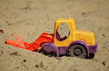Toy Plastic Bulldozer in the sand. A small digger on the playground