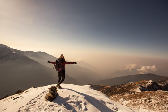 Female Traveller relaxing above clouds on top of snow high mountain and enjoying view of valley, freedom travel concept, nepali style hat, sunrise