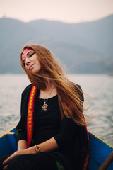 Fototapeta premium Portrait of Woman with misty make up and long red hair sitting in boat on mountain lake