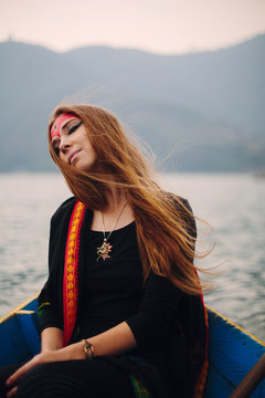 Portrait of Woman with misty make up and long red hair sitting in boat on mountain lake