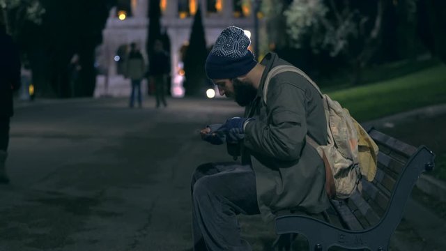 hungry beggar on bench at night counting his money
