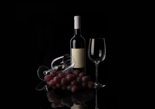 Red wine bottle, two empty wine glasses and grape on black background