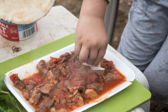 Meat goulash in a plate and a human hand with bread at a picnic