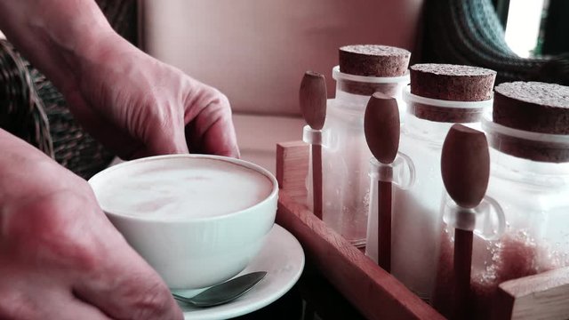coffee and bakery business, people and service concept, man or waiter is serving white hot coffee cup in a coffee shop - closeup at hand and sugar container set on a table