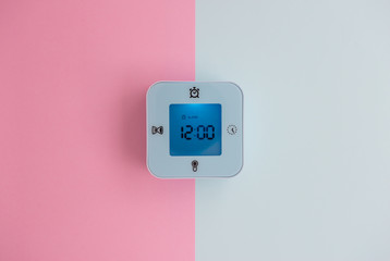 Minimal flat lay concept of blue mini digital alarm clock with blue light screen on the colorful pastel background - top view