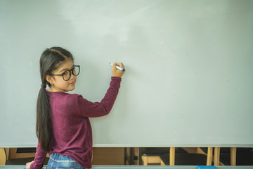 Asian girl writing on empty white board in class room at school