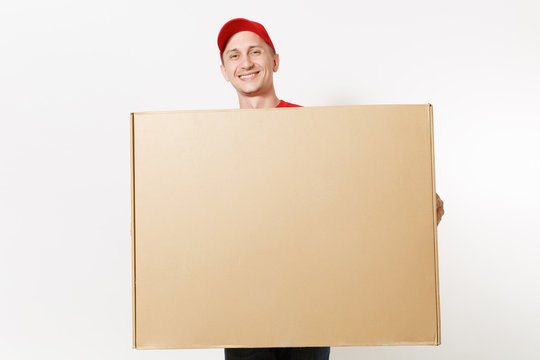 Delivery man in red uniform isolated on white background. Male in cap, t-shirt, jeans working as courier or dealer holding big large heavy empty blank cardboard box. Receiving package. Copy space area