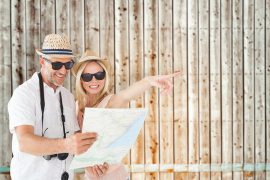Happy tourist couple using map and pointing against faded pine wooden planks
