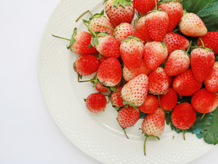 Close-up Fresh strawberries with green leaves on white plate against white background.