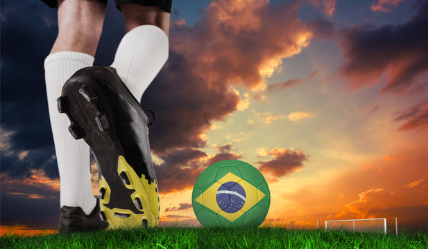 Composite image of football boot kicking brazil ball against green grass under dark blue and orange sky