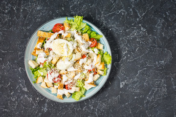 Fresh caesar salad in plate on dark stone table. Top view