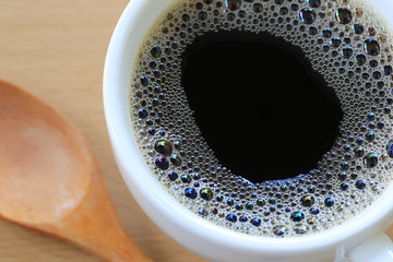Close Up in black coffee is in a white mug on a brown wooden floor background.